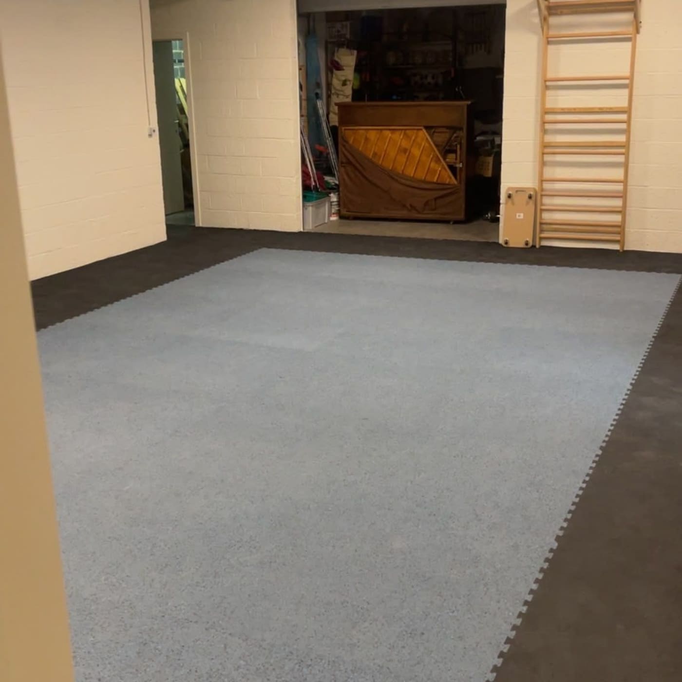Salle de sport adaptée après travaux — sol souple gris-bleu posé en dalles, espaliers muraux et faux plafond avec éclairage encastré